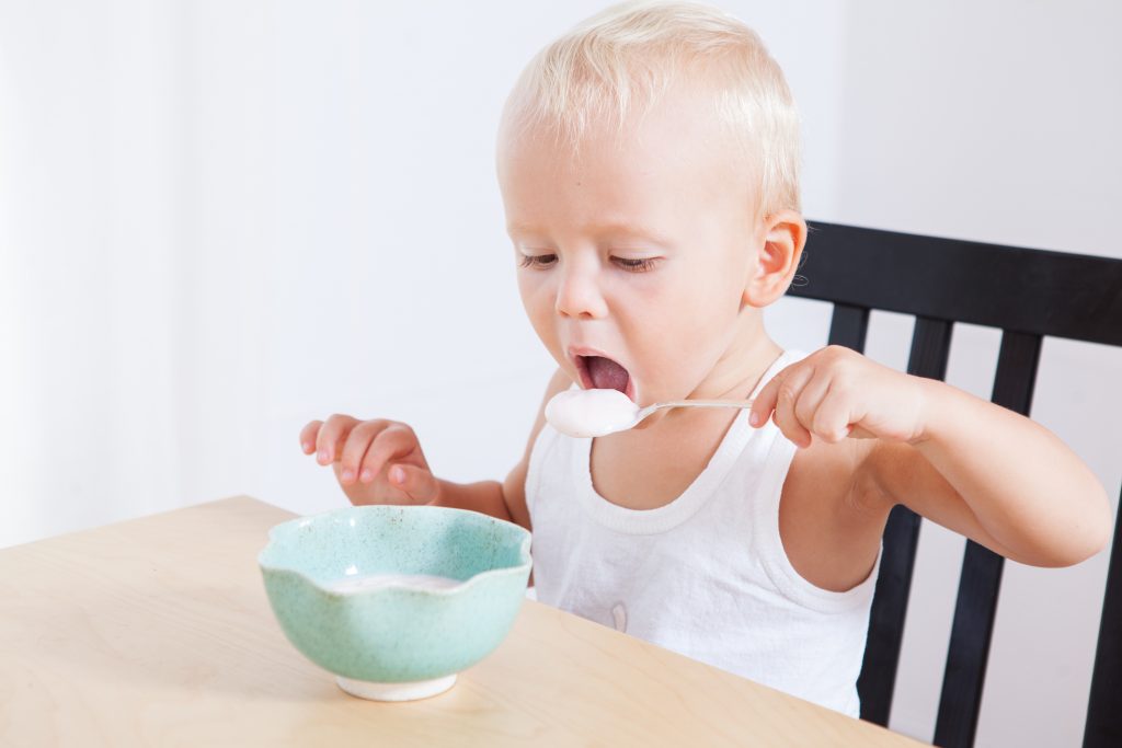 Little cute child boy eating yogurt himself, morning breakfast