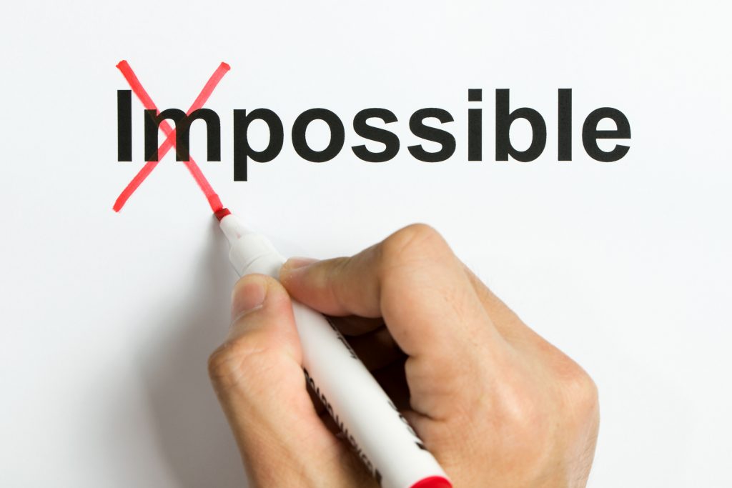 Hand holding marker pen to cross out the word impossible to reveal possible
