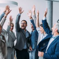 equipo de trabajadores están contentos y celebran juntos levantando los brazos